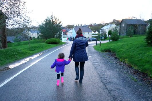 mother and daughter walking along road with grass next to it