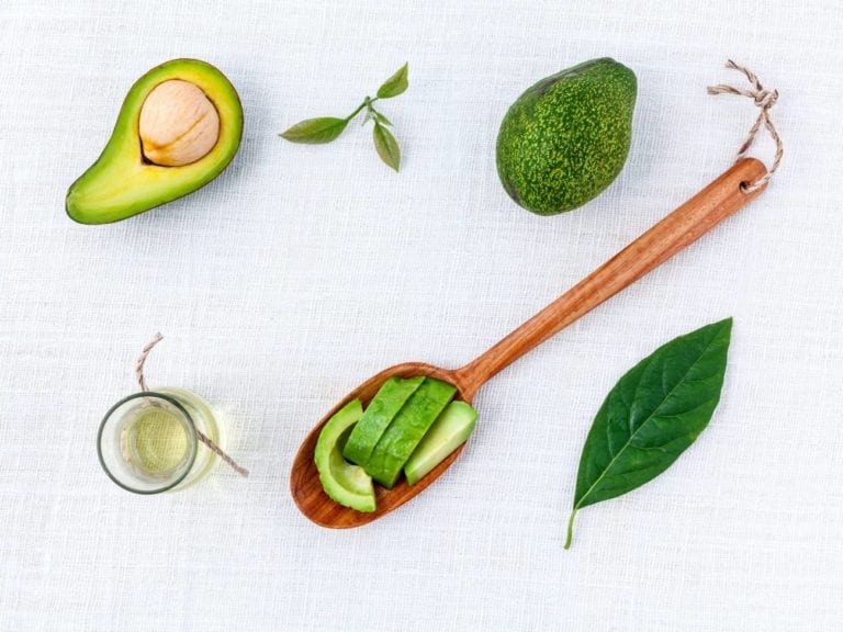 sliced avocado on wooden spoon with more avocadoes and a leaf next to it