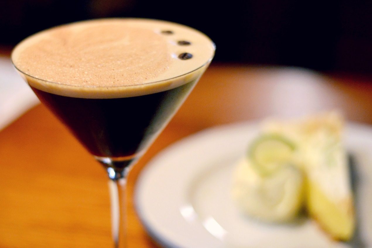 esperesso martini up close to camera and blurred dessert in background