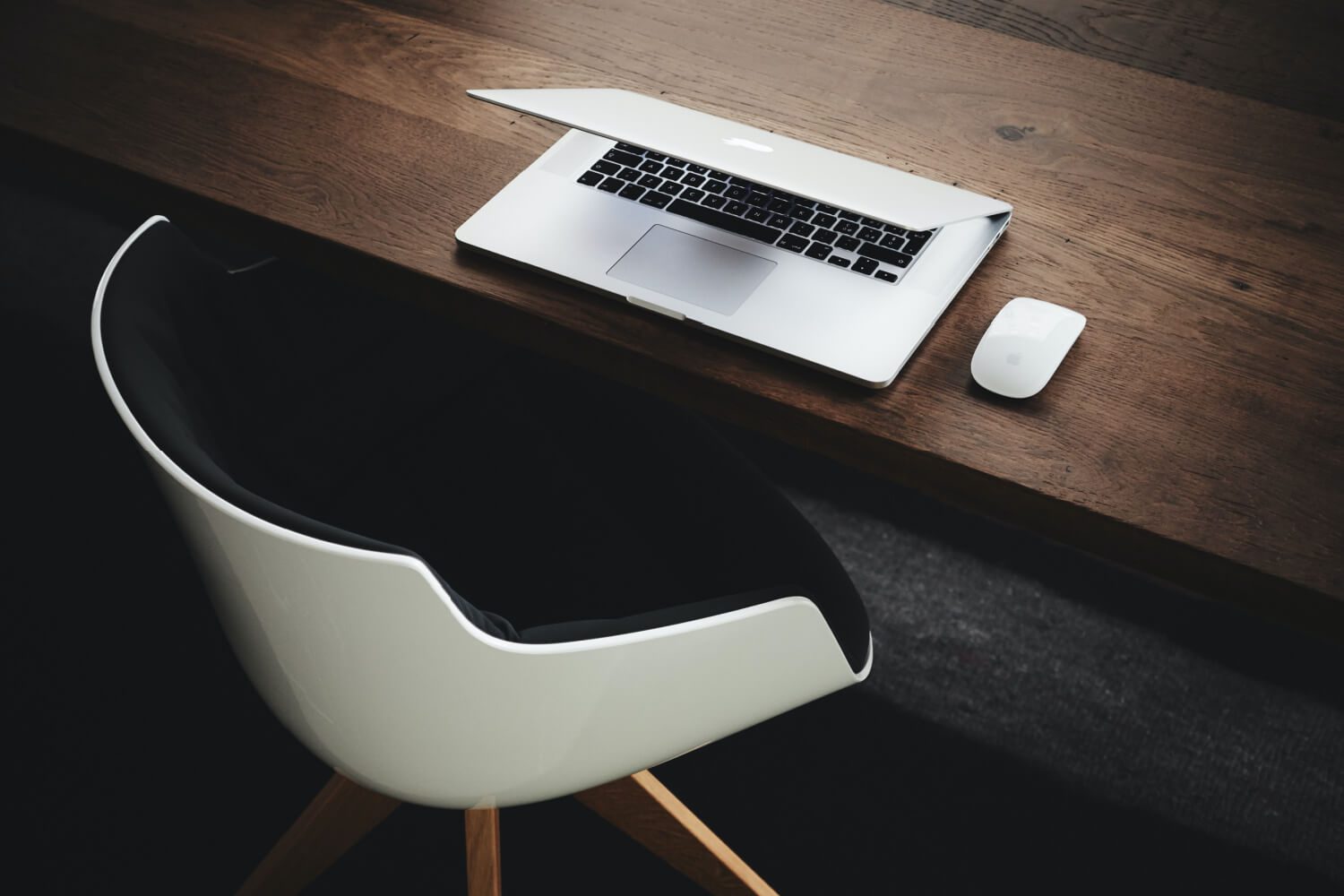 open laptop on brown wood desk next to white mouse, with white chair next to desk