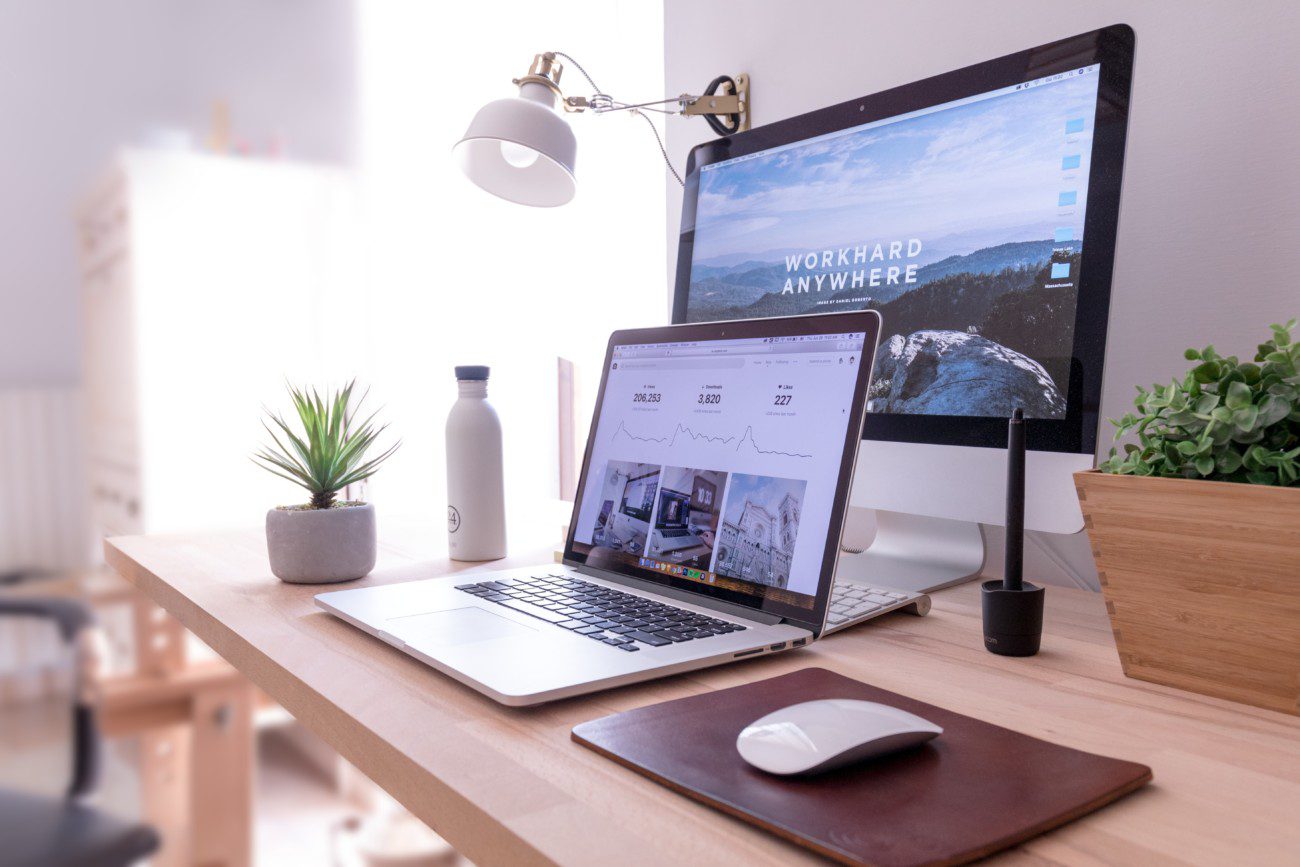 laptop and desktop on desk with words 'work hard anywhere' on screen and plant and white water bottle in background