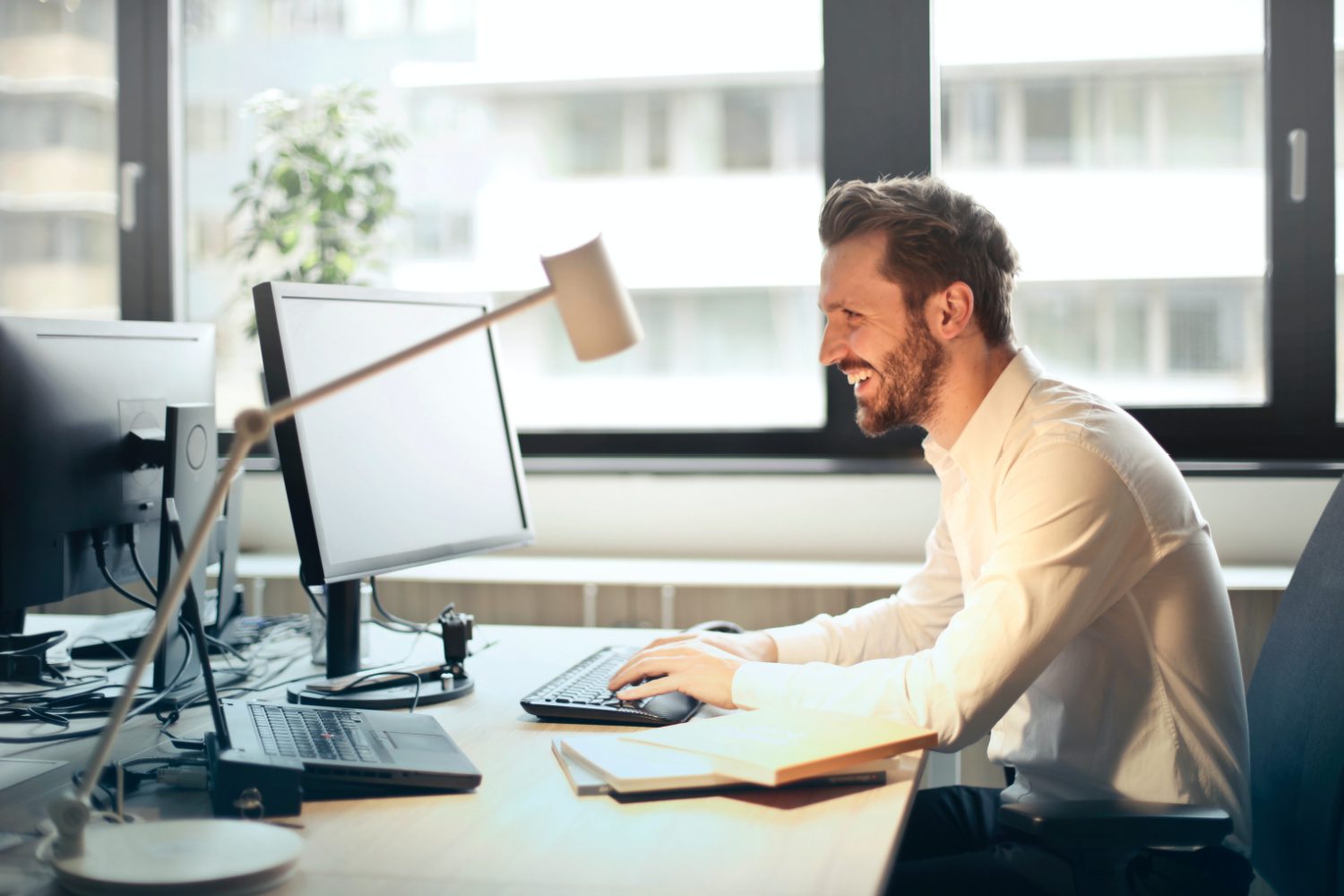 man sitting at desk with computer in front of him and smiling