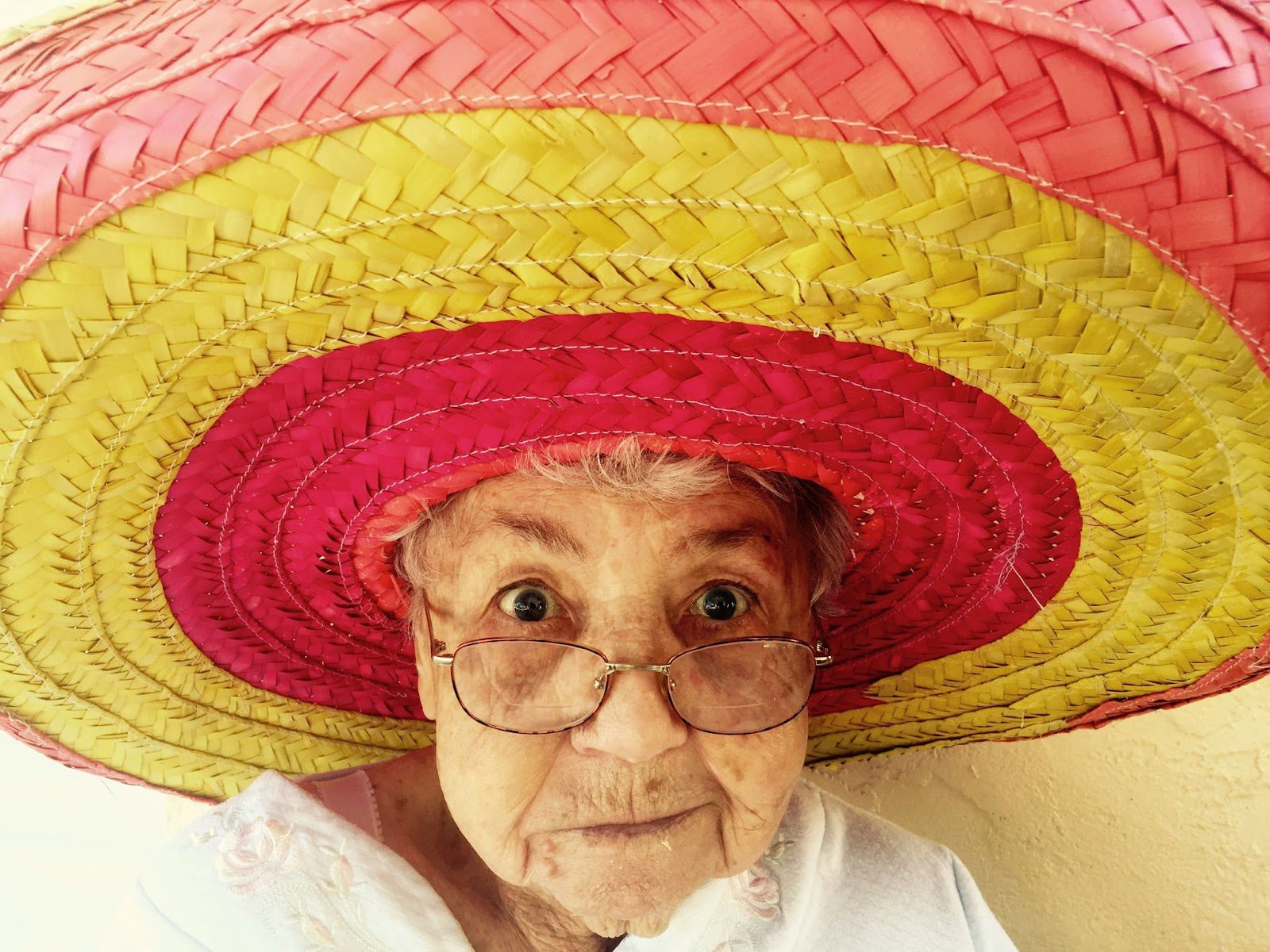 old lady wearing big red and yellow Mexican hat and smiling cheekily