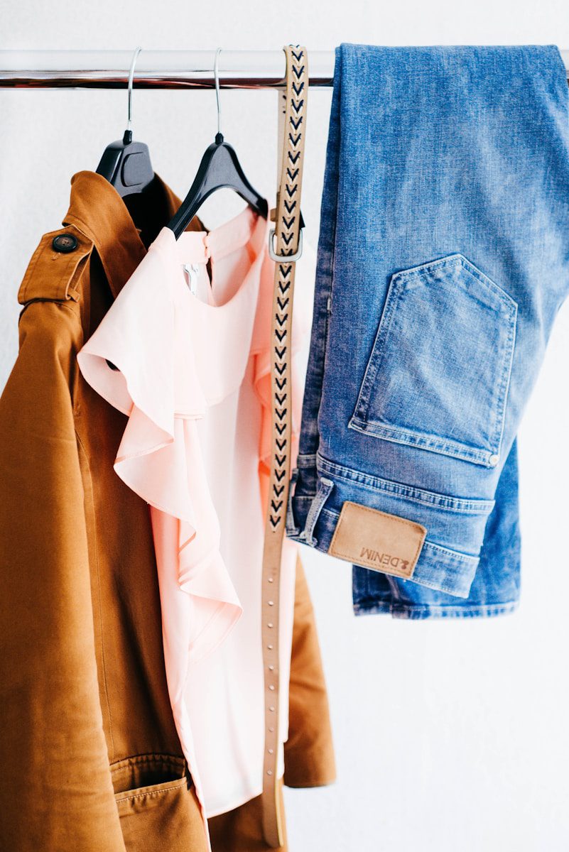 women's clothing - jeans, top, jacket and belt hanging on clothes rack