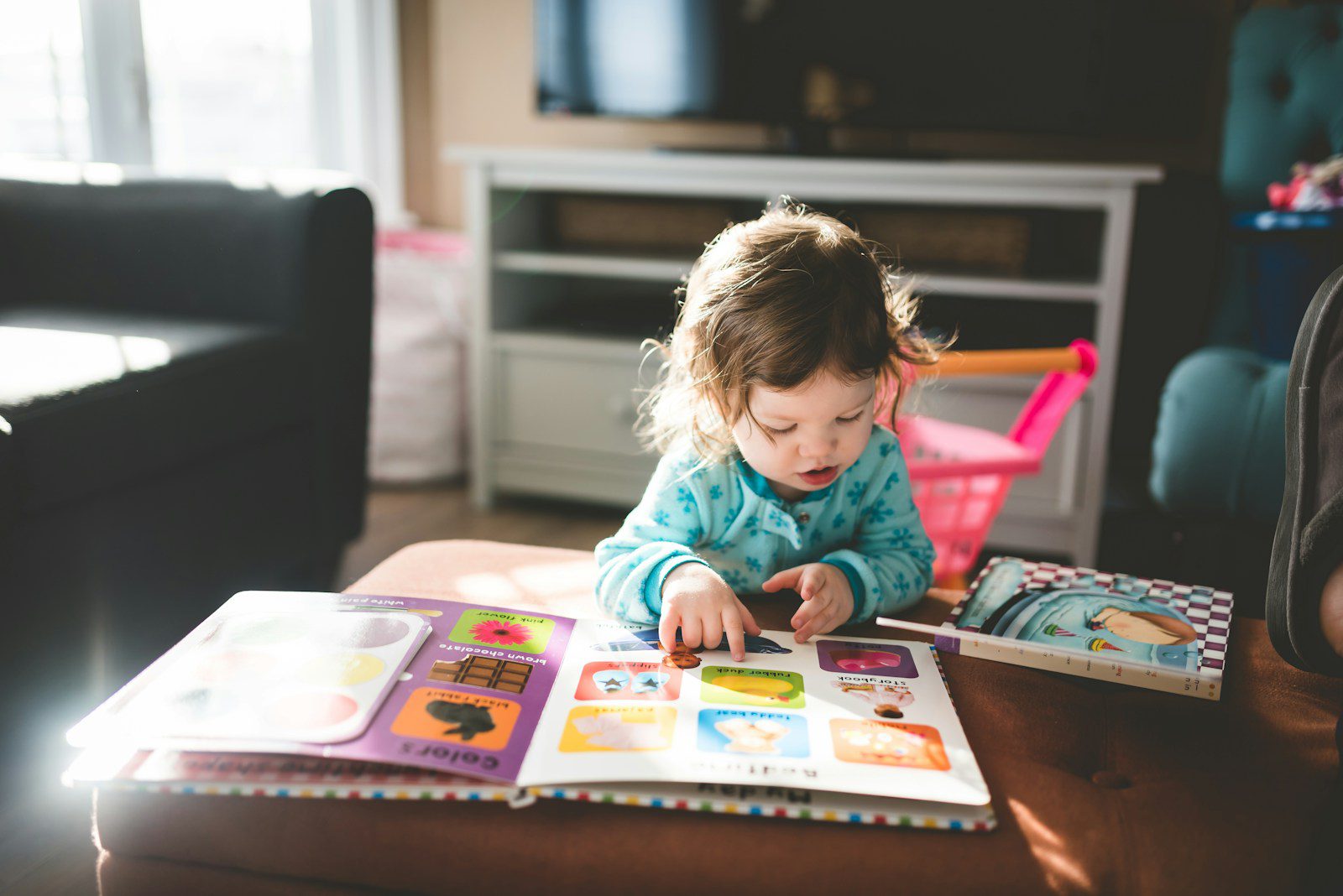 young child reading picture book in lounge with toy trolley behind her