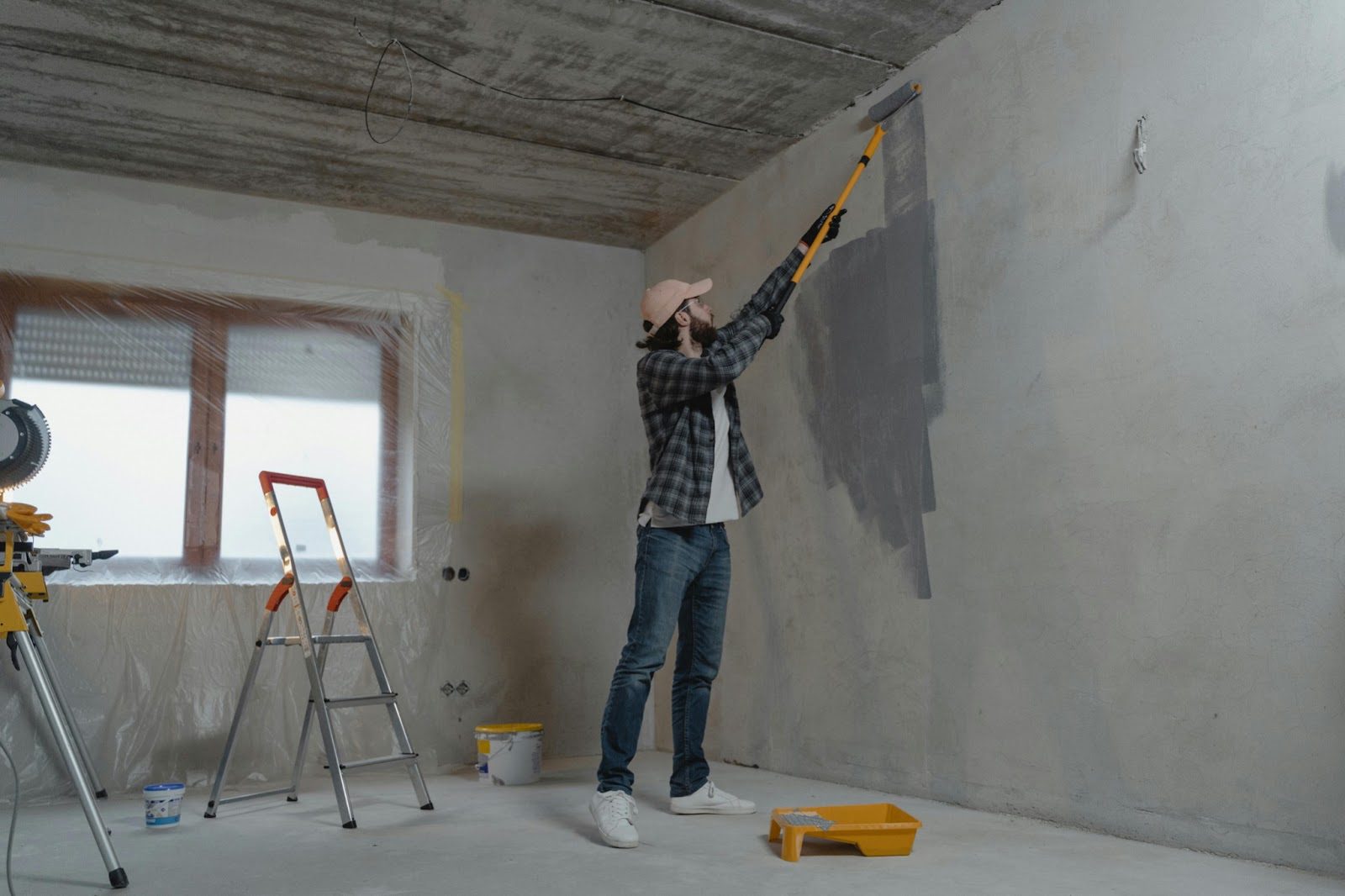 man painting wall grey next to small ladder and window