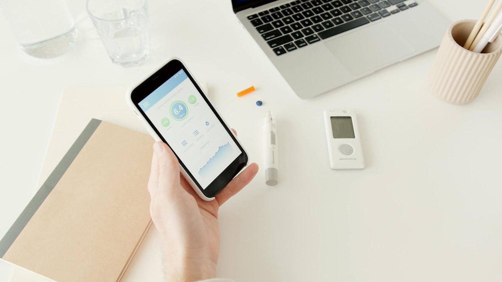 hand holding phone with lapotop in background and health monitor