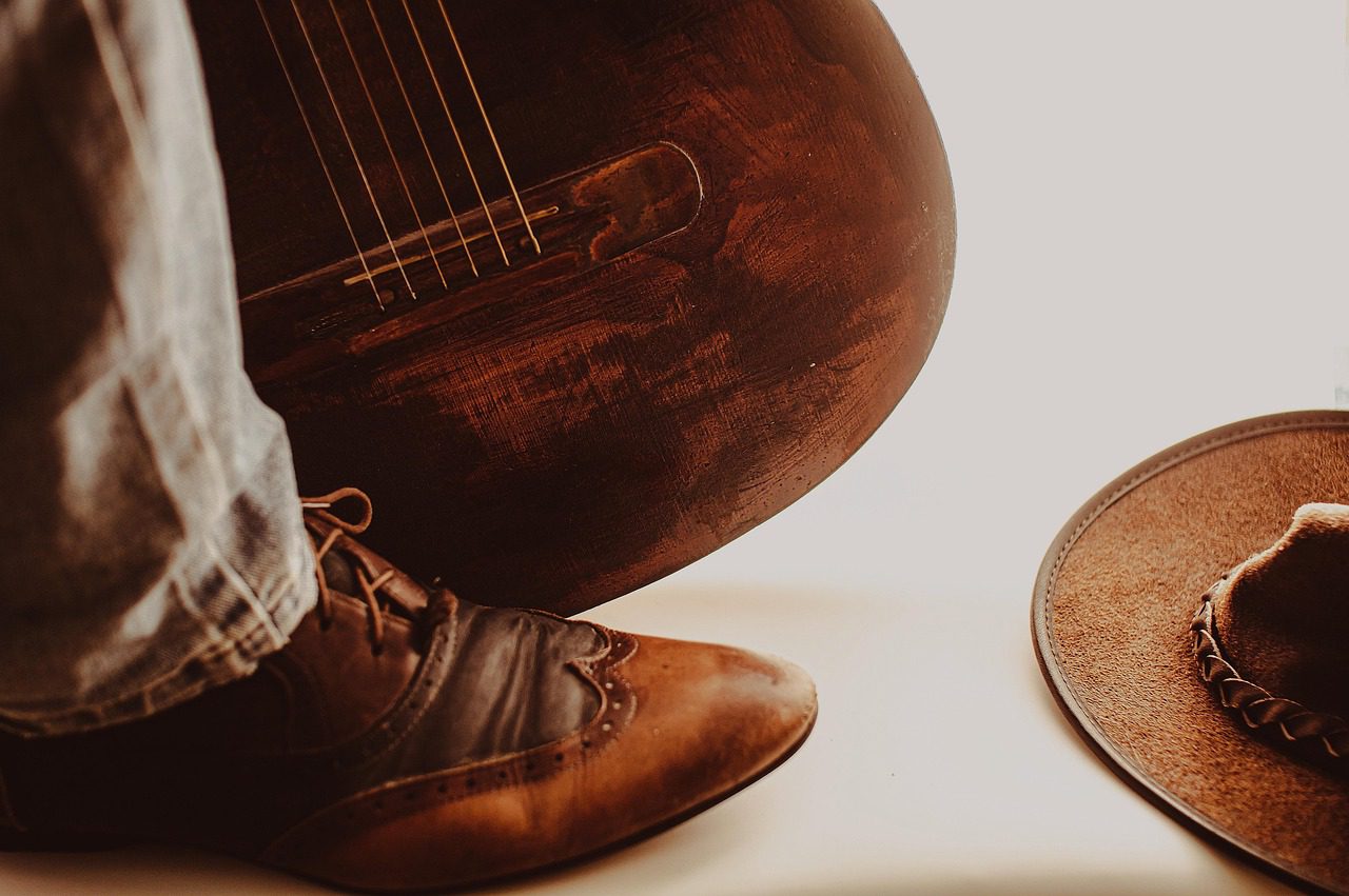 brown shoe on person's foot next to brown guitar
