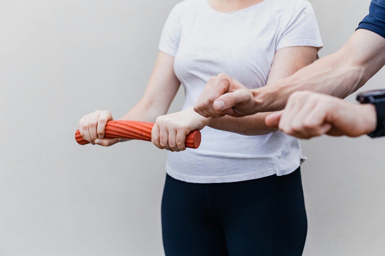 a woman gripping a red weight while standing next to a man showing her how to grip it