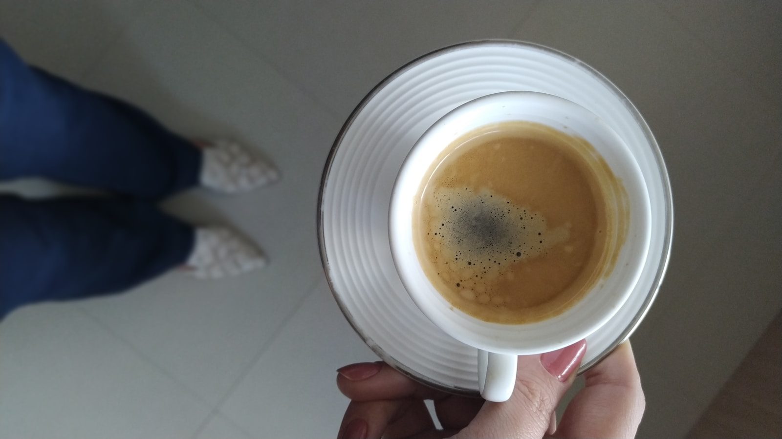 white cup with coffee in it on saucer from above in someone's hand, with person standing nearby
