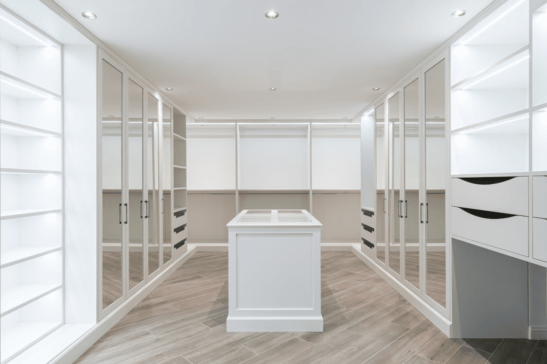 walk in wardrobe with mirrored doors along sides and white unit in centre of room