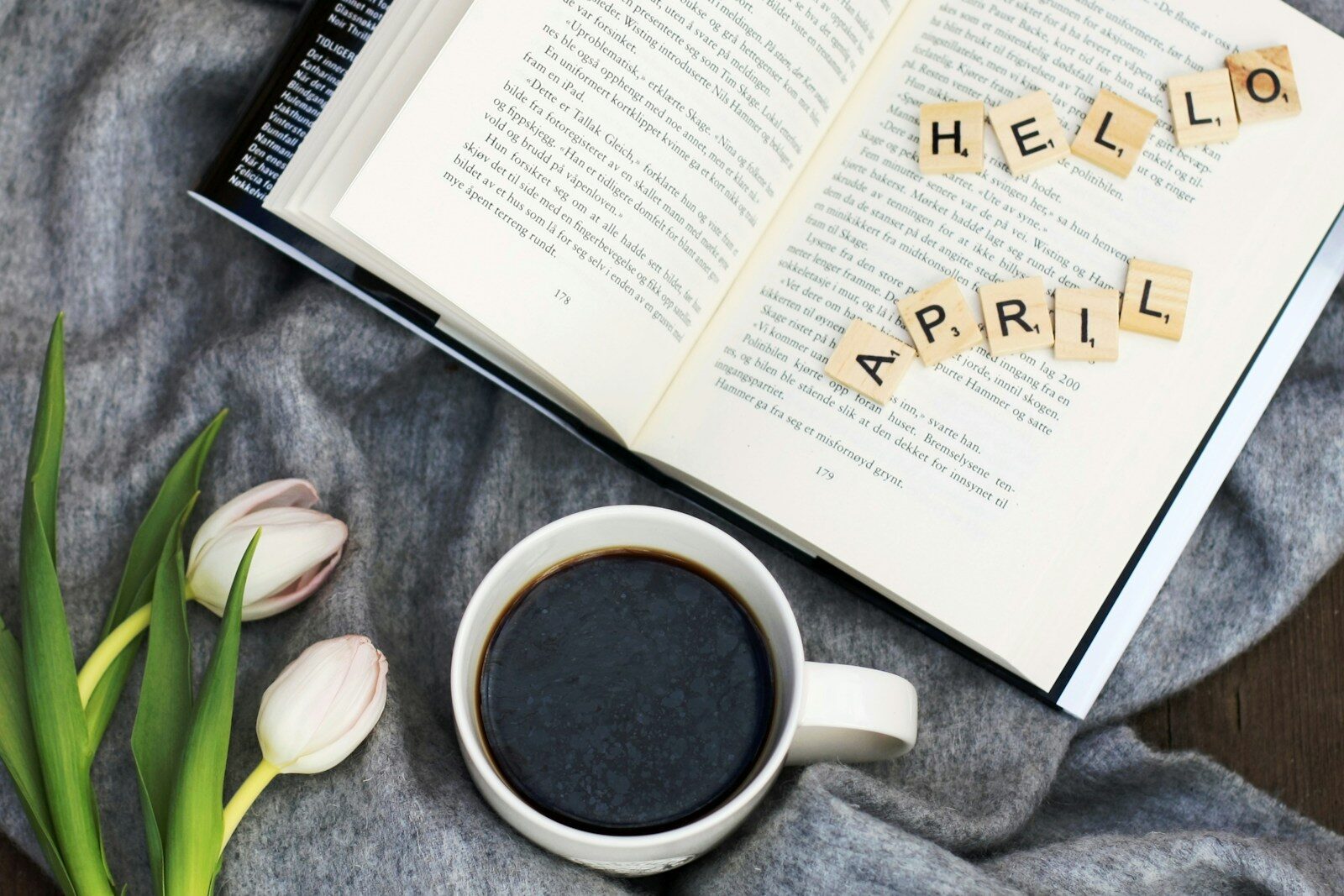 a cup of coffee next to an open book with scrabble tiles saying hello april on the book