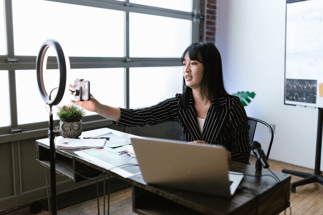 woman sitting at desk with phone attached to ring light